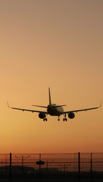 Vertical Screen: A stunning scene unveils as a plane smoothly touches down at dusk against a vibrant orange sunset backdrop, encapsulating the essence of aviation, travel, and the expansive skies