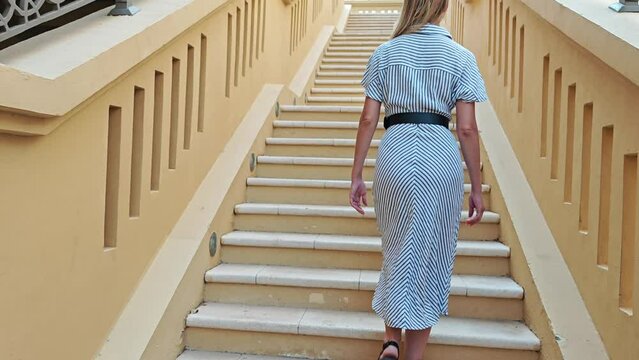Young woman climbs the stairs and suffers from lower back pain