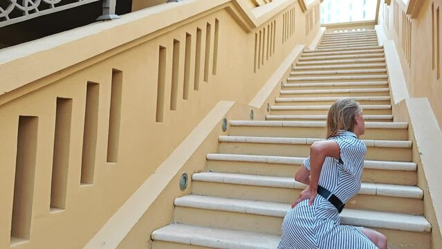 Young woman climbs the stairs and suffers from lower back pain