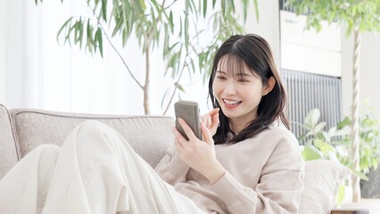 ソファでくつろぎながらスマホを見る女性