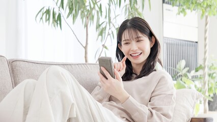 ソファでくつろぎながらスマホを見る女性