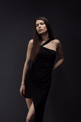 A sophisticated woman poses in a sleek black dress, exuding elegance and confidence against a dark studio backdrop. Perfect representation of fashion and style.