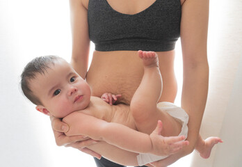 Sporty Asian woman with stretch marks after childbirth holds her baby boy. Close up view.