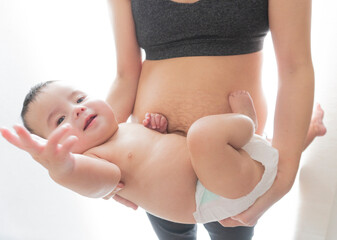 Sporty Asian woman with stretch marks after childbirth holds her baby boy. Close up view.