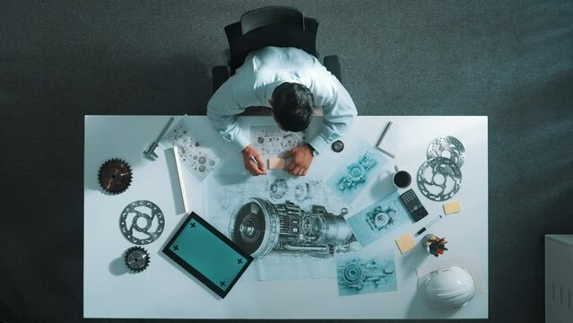 Top down view of skilled engineer writing and planning turbine engine design while sitting at meeting table with gear and electronic generator scatter around. Technician taking a note. Alimentation.