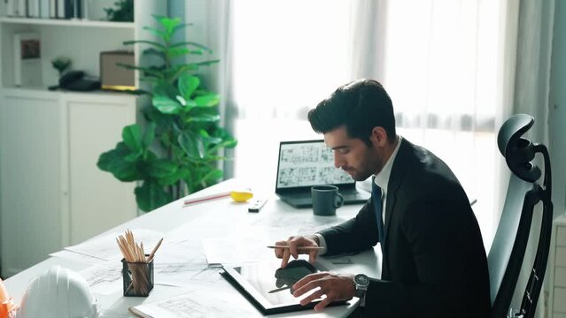 Architect engineer using laptop planning house design at office while sitting at meeting table with blueprint and equipment scatter around.Skilled civil engineer working at blueprint. Alimentation.