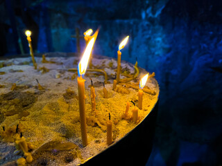 Lit candles in sand filled candle holder in church against dark wall. Religious or spiritual...