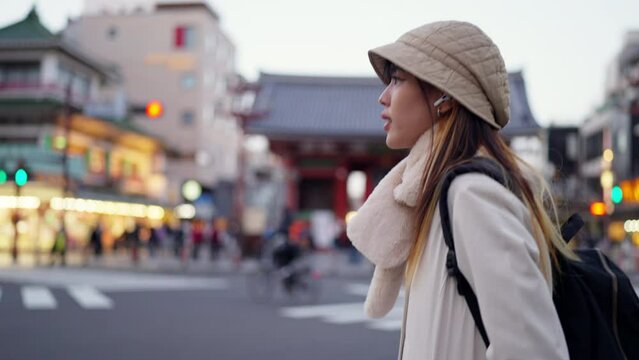 4K Young Asian woman walking on city street crosswalk and looking cityscape building in Tokyo, Japan. Attractive girl traveler enjoy urban outdoor lifestyle travel in Japan on winter holiday vacation.