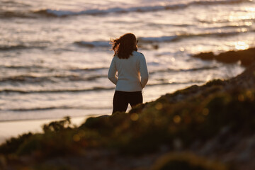 Woman walking along the beach at sunset in Sagres, Algarve, Portugal