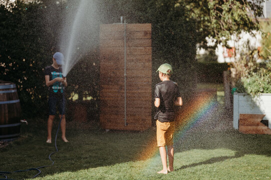 Two brothers playing with water in a backyard on a sunny day