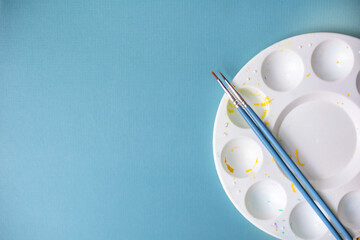 artist palette with paint brushes against blue background copy space