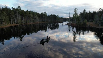 Two people canoe on peaceful pond in northern Maine woods