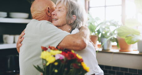 Senior, couple and hug with flowers in home for anniversary gift, celebration and love in marriage. Elderly, people and happy with embrace or bouquet in kitchen for romance, support or valentines day