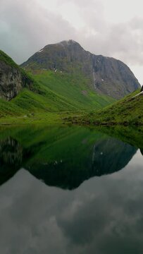 Norweigan Fjords Stavbergvatnet Urke, In the heart of a valley, a lake encircled by towering mountains, creating a serene and picturesque natural landscape with lush green grass and plants all around