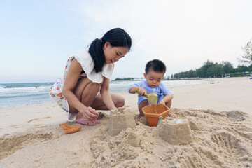Asian mother and son playing sand and toy on beach