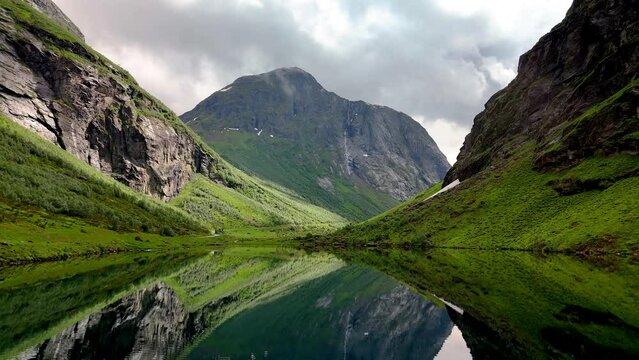 Norweigan Fjords Stavbergvatnet Urke, In the heart of a valley, a lake encircled by towering mountains, creating a serene and picturesque natural landscape with lush green grass and plants all around