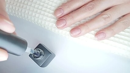 Gel polish manicure step-by-step video tutorial. Step 7 Nails base coat. A woman is shown in a close-up applying a base coat of polish to her fingernails