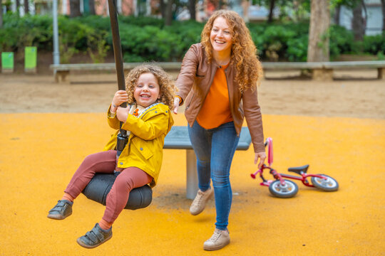 Mother pushing a kid on a swing in a playground