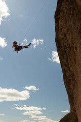 A woman is hanging from a rope on a cliff. Concept of adventure and excitement, as the woman is...