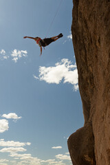 A man is hanging from a rope on a cliff. The man is in the air and he is in a free fall