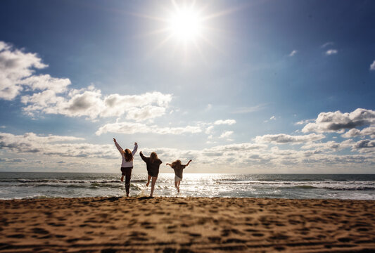 Three young girls running and jumping on sunny beach