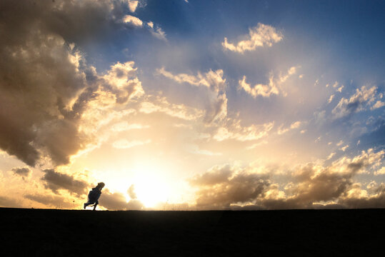 Silhouette of young girl running against big beautiful sky
