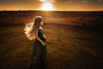 Profile of beautiful young girl standing on hill at sunset