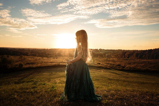 Beautiful young girl standing on grassy field at sunset