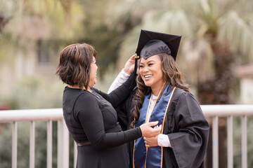 Mother putting cap on duahgter for her graduation, both laughing