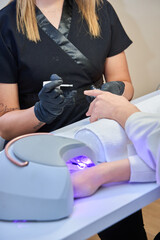 unrecognizable woman drying freshly painted gel nails with an ultraviolet lamp in a beauty salon