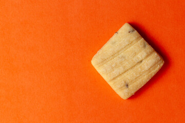On an orange background, A piece of sweet and salted Cumin Cookie or Indian Jeera Cookie. Top-down view. Food Flat lay.