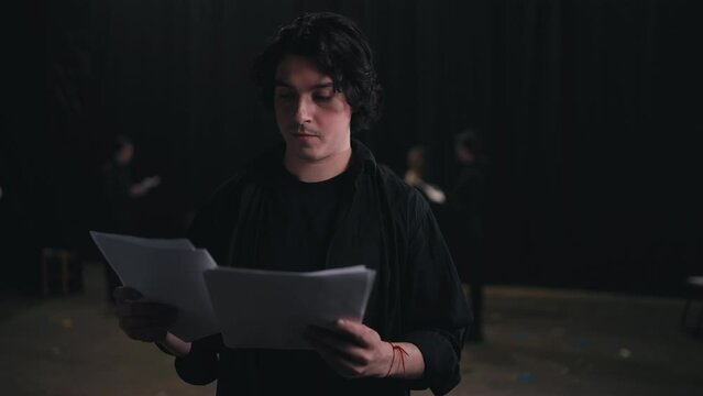 Portrait of a confident Happy man with medium-length brunette hair in a black suit an actor who holds a piece of paper in each of his hands and reads the text of your character and the script of the