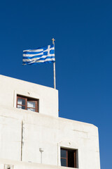 Fototapeta premium Greek flag on the building in a blue summer sky. Copy space.