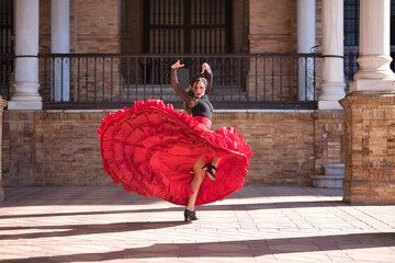 Young, beautiful, brunette woman in black shirt and red skirt, dancing flamenco between marble columns in Spain square in Seville. Flamenco concept, dance, art, typical Spanish.