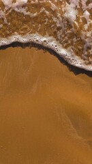 A white foam topped wave pours over smooth golden sand.