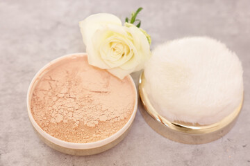 Face powder, puff applicator and rose flower on grey textured table, closeup