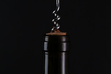 Wine bottle with corkscrew on black background, closeup