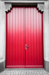 Bright red door at the black and white entrance area. Old entrance to a church.
