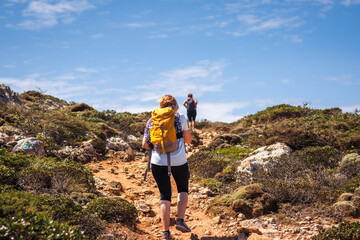 Two female hikers with backpack walking up to cliffs on Algarve coastline in Portugal. Active...