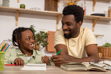 Naklejka premium Cheerful black dad with his daughter doing school tasks