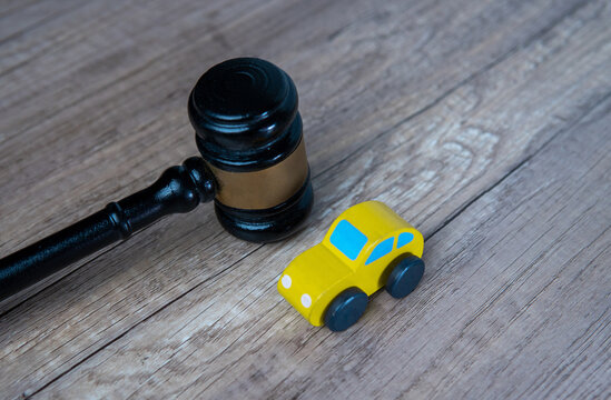 A close-up image of a yellow toy car and a wooden judge's gavel on a wooden table. Transport law, lemon law concept.
