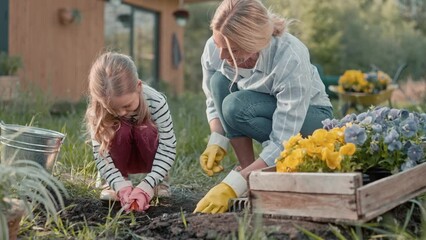 Pretty family working together during sunny day. Cute blond daughter with gardening tool digging hole for planting. Loving mother looking at work process and smiling. Teamwork.