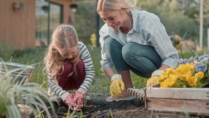 Happy family having leisure day in garden. Pretty woman with her cute child preparing ground for planting flowers. Cultivating black soil with gardening tools. Spending time usefully.