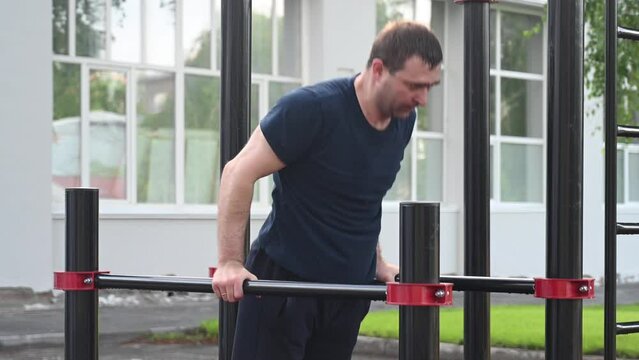 Middle-aged man doing push-ups on parallel bars outdoors. 
