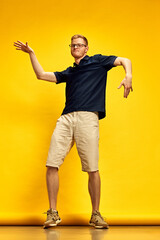 Full-length image of emotional young man in smart casual clothes cheerfully dancing against bright yellow background. Positive vibe. Concept of human emotions, facial expression, lifestyle
