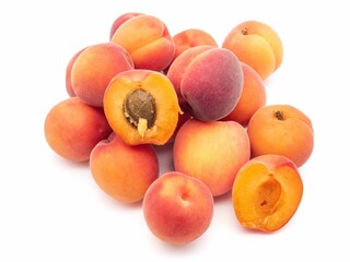 Pile of fresh apricots with some cut open showing the seed inside on a white background.