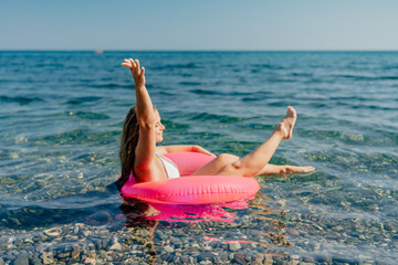 A woman is floating on a pink inflatable raft in the ocean