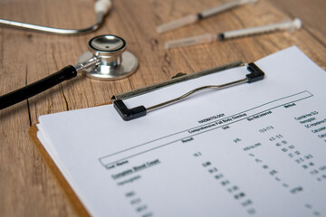 A close-up image of a clipboard with a hematology medical report and a stethoscope on a wooden table.