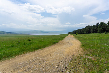 A gravel road along a green field leading into the distance between the Tsalka reservoir and a...
