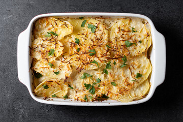 Potato gratin baked with cream and cheese on black slate background. Top view